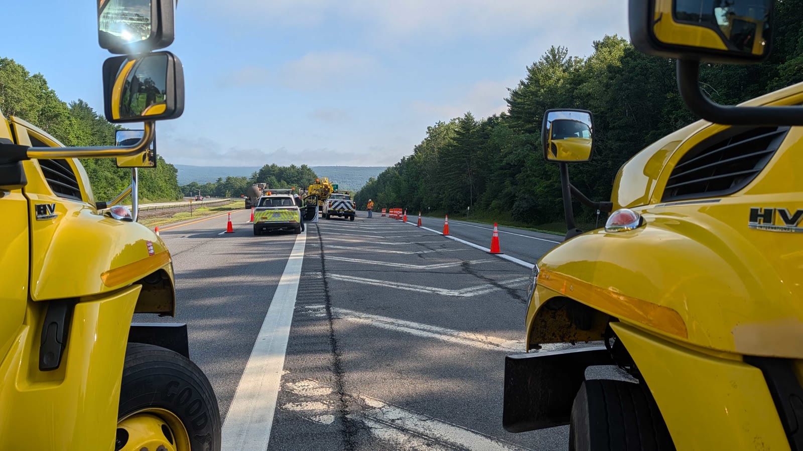 Two New York State Thruway trucks framing an active lane closure, with cones and a crew working ahead