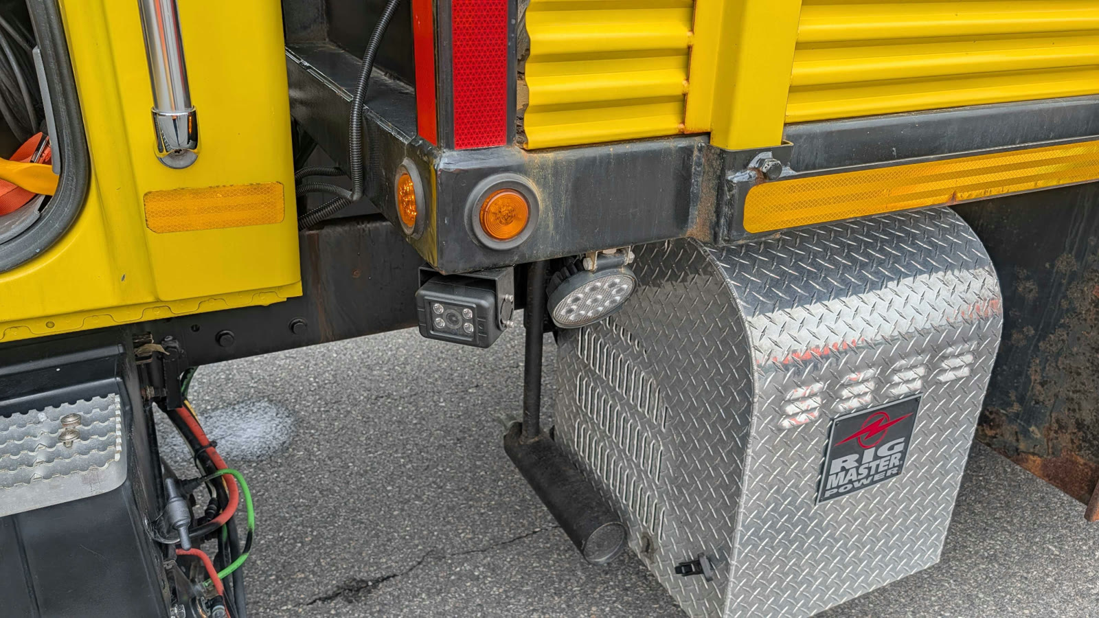 An industrial detection camera mounted under the rear of a yellow highway work truck